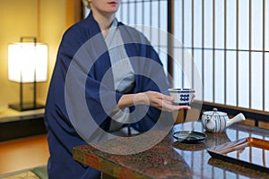 Young caucasian woman in Japanese clothes sitting at the table in ryokan room drink a tea