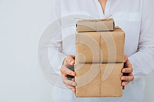 Young caucasian woman in jeans shirt holds in hands stacked gift boxes wrapped in brown craft paper tied with twine. Christmas