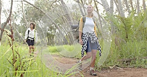 Young Caucasian woman leads the way on a forest hike, with a young biracial woman following