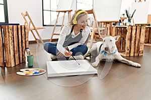 Young caucasian woman listening to music drawing with dog at art studio
