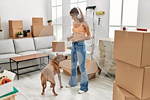 Young caucasian woman listening to music feeding dog at home