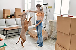 Young caucasian woman listening to music feeding dog at home