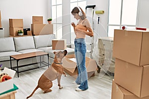 Young caucasian woman listening to music feeding dog at home