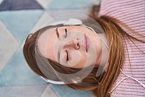 Young caucasian woman listening to music lying on floor at home