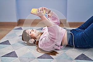 Young caucasian woman listening to music lying on floor at home