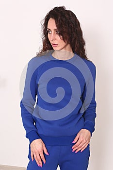 young caucasian woman with long curly brown hair in blue hoodie suit closeup photo on white wall background