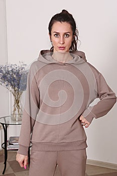 young caucasian woman with long curly brown hair in brown hoodie suit closeup photo on white wall background