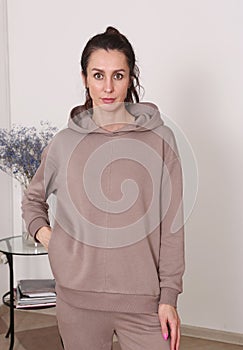 young caucasian woman with long curly brown hair in brown hoodie suit closeup photo on white wall background