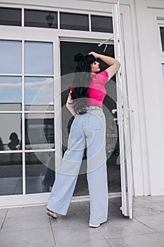 young caucasian woman with long dark wavy hair poses for the camera near the door in warm weather