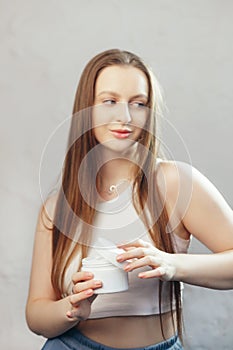 Young caucasian woman with long flowing hair is opening unbranded white jar with cosmetic cream