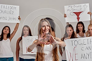 Young caucasian woman with long hair showing heart or love sign, smiling at camera. Group of diverse women holding