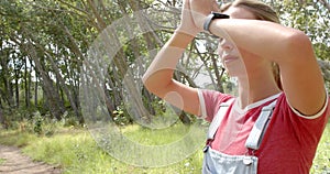 Young Caucasian woman looks into the distance with binoculars, surrounded by greenery