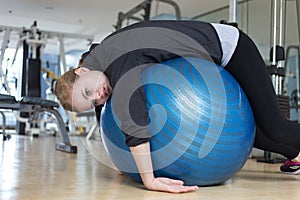 Young caucasian woman lying on blue gymnastic ball looking exhausted, tired, bored and weary at the gym