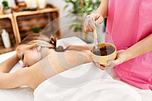 Young caucasian woman lying on table having back chocolate treatment at beauty salon