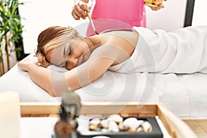 Young caucasian woman lying on table having back chocolate treatment at beauty salon