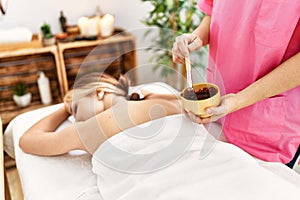 Young caucasian woman lying on table having back chocolate treatment at beauty salon