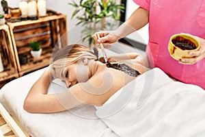 Young caucasian woman lying on table having back chocolate treatment at beauty salon