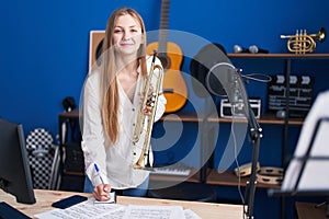 Young caucasian woman musician composing song holding trumpet at music studio