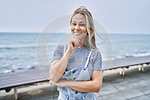 Young caucasian woman outdoors looking confident at the camera smiling with crossed arms and hand raised on chin