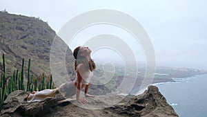Young Caucasian woman performing upward facing dog pose outdoorsThe woman sitting on the edge of a cliff in the pose of