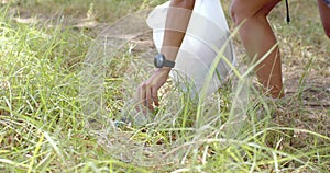 A young Caucasian woman is picking up a plastic bottle from the grass, collecting trash