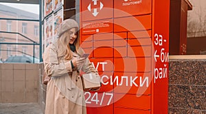 Young caucasian woman picks up mail from automated self-service post terminal machine after online shopping