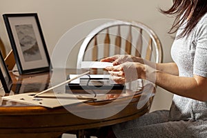 A young caucasian woman is placing a printed photograph into a picture frame with kickstand.