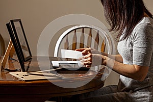 A young caucasian woman is placing a printed photograph into a picture frame with kickstand.