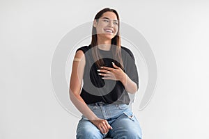Young Caucasian woman with plaster bandage after covid-19 vaccine injection smiling, feeling happy on light background