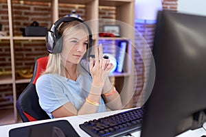 Young caucasian woman playing video games wearing headphones holding symbolic gun with hand gesture, playing killing shooting