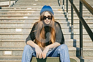Young caucasian woman posing on street with skateboard in hands. Teenager girl in blue jeans extreme sports in an urban