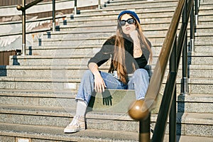 Young caucasian woman posing on street with skateboard in hands. Teenager girl in blue jeans extreme sports in an urban