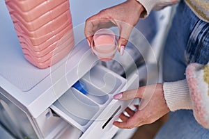 Young caucasian woman pouring detergent on washing machine at laundry room