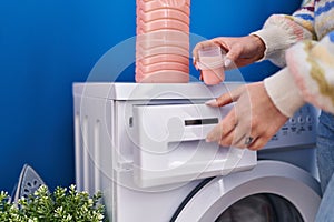 Young caucasian woman pouring detergent on washing machine at laundry room