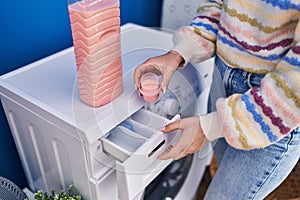 Young caucasian woman pouring detergent on washing machine at laundry room