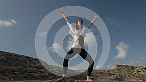 Young caucasian woman practising yoga on the rocky beach