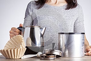 A young caucasian woman is preparing coffee on table using a percolator filter papers and a jar of coffee