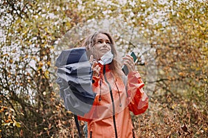 Young caucasian woman putting on a coronavirus mask in the autumn forest.