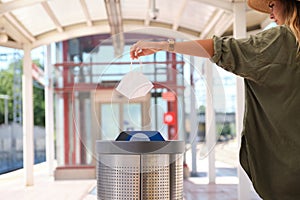 Young caucasian woman putting used dirty surgical mask into a garbage bin