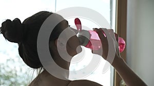 Young caucasian woman quenching her thirst. female drinks water from pink bottle