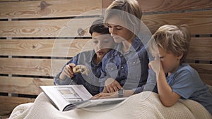 Young caucasian woman reads a book to two sons sitting on the floor. A beautiful young mother is reading a book