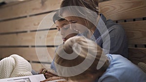 Young caucasian woman reads a book to two sons sitting on the floor. A beautiful young mother is reading a book