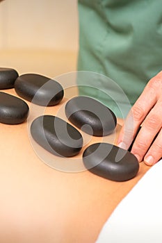 Young caucasian woman receiving back massage with black stones by masseur in spa salon. A woman getting a spa treatment.