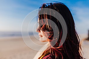 Young caucasian woman relaxing at the beach at sunset. Selective focus on hair flying on a windy day. Holidays and relaxation