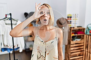 Young caucasian woman at retail shop doing ok gesture shocked with surprised face, eye looking through fingers