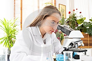 Young Caucasian woman scientist looking through a microscope in a laboratory for doing research. Students analyze biochemical.