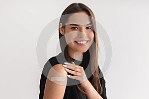 Young Caucasian woman showing shoulder with band aid after coronavirus vaccination, promoting covid-19 immunization