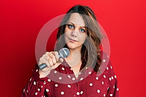 Young caucasian woman singing song using microphone thinking attitude and sober expression looking self confident