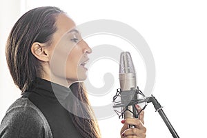 Young Caucasian woman singing or speaking to mic in music or radio studio