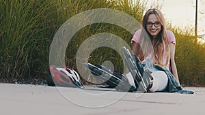 Young caucasian woman siting on the trail in the park with rollerblades during the sunset. Sport and recreation concept